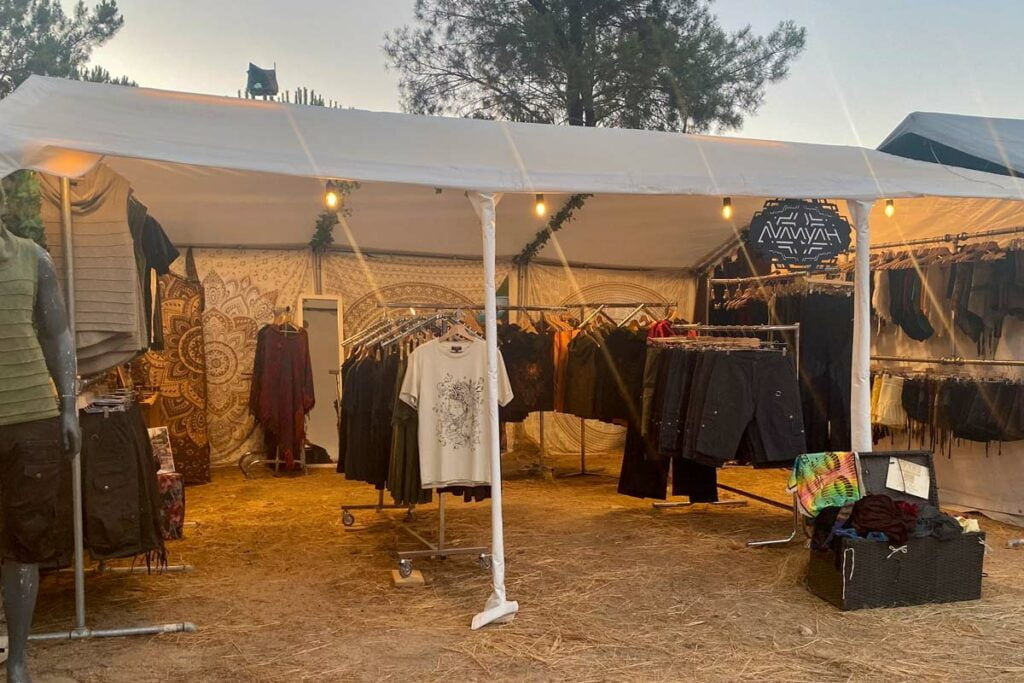 Shoppers exploring Avanyah's booth at a European psychedelic trance festival, featuring alternative clothing, festival fashion, and art wear.