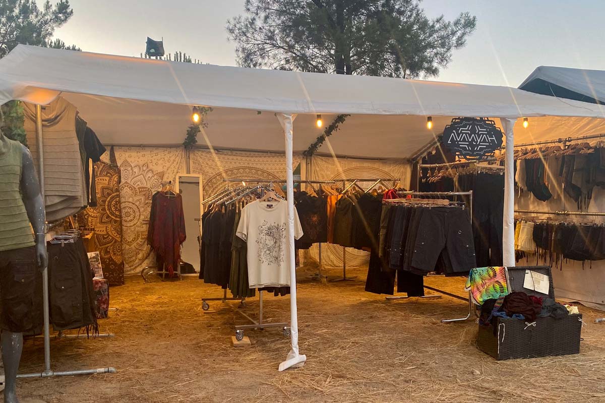 Shoppers exploring Avanyah's booth at a European psychedelic trance festival, featuring alternative clothing, festival fashion, and art wear.